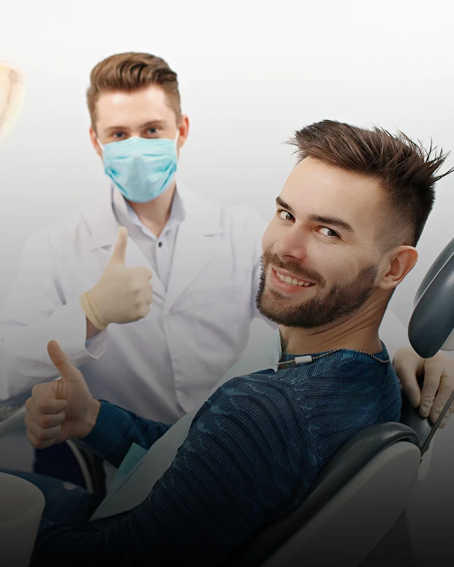 A patient sitting in a dental exam chair and turning over his shoulder to give the camera a thumbs up